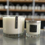 Two candles with 'LIT' branding on a metallic surface with shelves in the background.